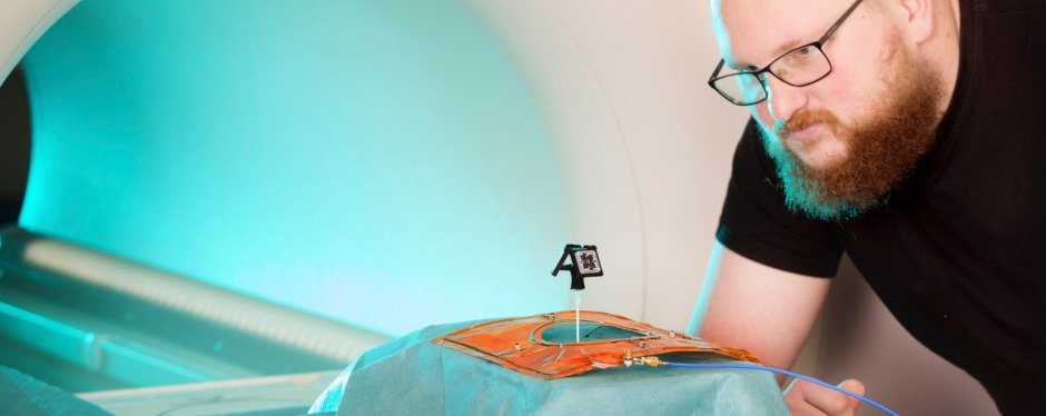 A man looks at a small technical device standing on the table of an MRI machine.