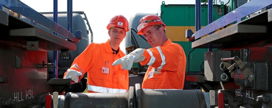 Two workers in protective clothing inspect container wagons.